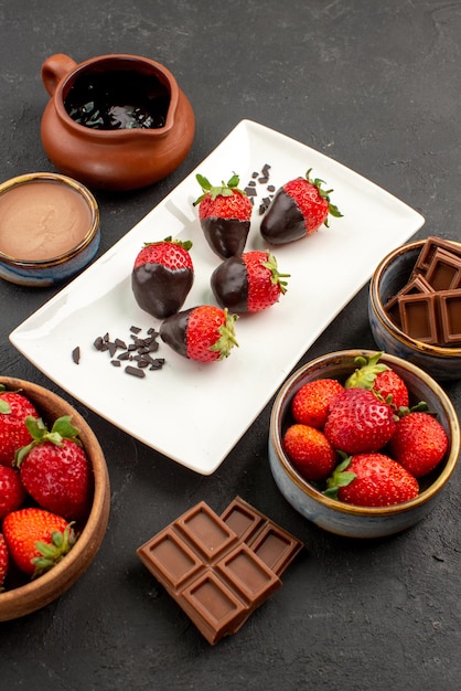 Foto gratuita vista laterale da lontano crema al cioccolato crema al cioccolato e fragole in una ciotola fragole ricoperte di cioccolato sul piatto al centro della tavola nera