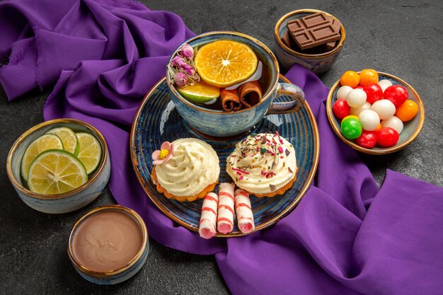 遠くからの側面図一杯のお茶青い一杯のお茶とレモンシナモンスティックチョコレートキャンディーのボウル柑橘系の果物とチョコレートクリームのスライス