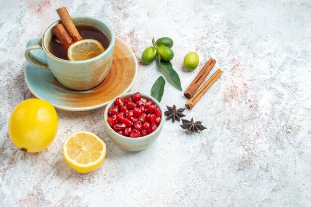 Side view from afar a cup of tea lemon seeds of pomegranate star anise and cinnamon sticks next to the cup of tea with lemon and cinnamon on the table