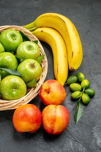 Вид сбоку издалека, корзина с фруктами, зелеными яблоками, лаймами, нектаринами и бананами на столе