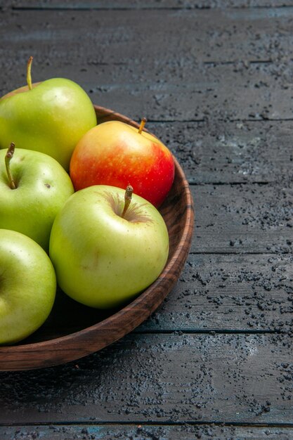 Вид сбоку издалека зелено-желто-красноватых яблок деревянная миска зелено-красно-желтых яблок на левой стороне деревянного стола