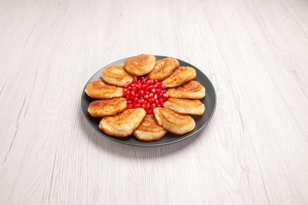 검은 접시에 석류 팬케이크와 석류 씨앗이 있는 멀리 있는 팬케이크의 측면 보기