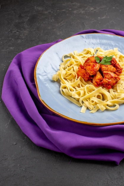 Vista laterale da lontano la pasta sul piatto da tavola di appetitoso sugo di carne di pasta ed erbe aromatiche sulla tovaglia sul tavolo scuro