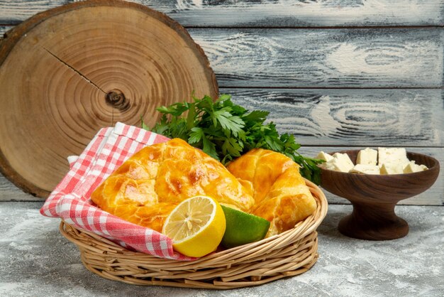 Side view from afar pies and lemon pies herbs lemon and lime and tablecloth in the basket plate of cheese and cutting board on the wooden background