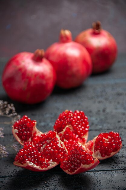 Side view from afar pomegranate on table red pilled pomegranate next to three pomegranates on dark background