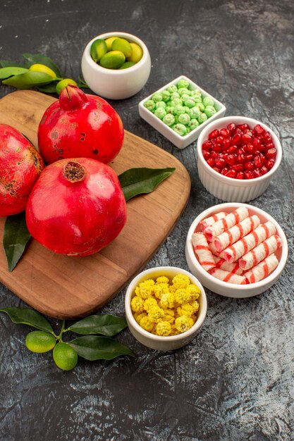 Side view from afar pomegranates bowl of sweets limes pomegranates with leaves on the cutting board