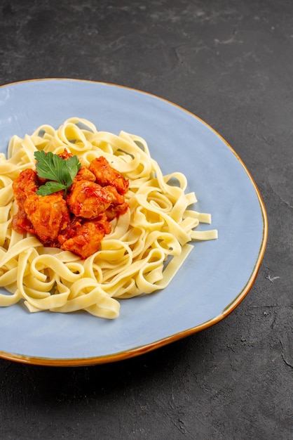 テーブルの上に肉と肉汁が入ったおいしいパスタの遠くのおいしい食べ物の青いプレートからの側面図