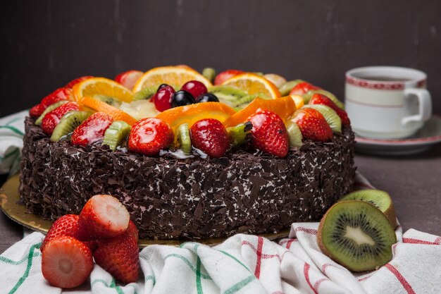 Side view fruit cake with strawberry and kiwi and cup of tea in rag napkins