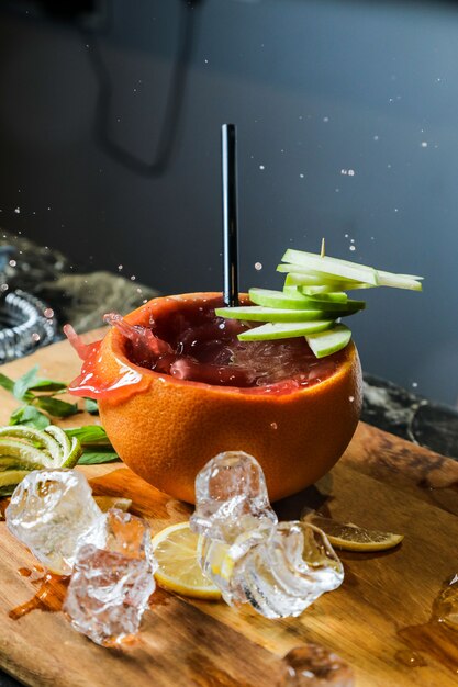 Side view fruit cocktail in orange peel with apple and lemon wedges on a cutting board