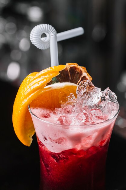 Side view fruit cocktail with slice of orange ice and straw on the glass