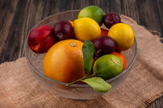 Side view fruit mix lemons  limes  plums  peaches and oranges in a vase on a beige napkin