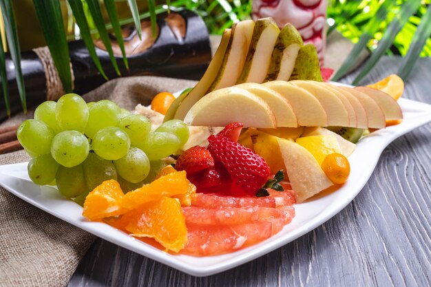 Side view fruit plate orange strawberry banana kiwi pear grapes and cherry plum