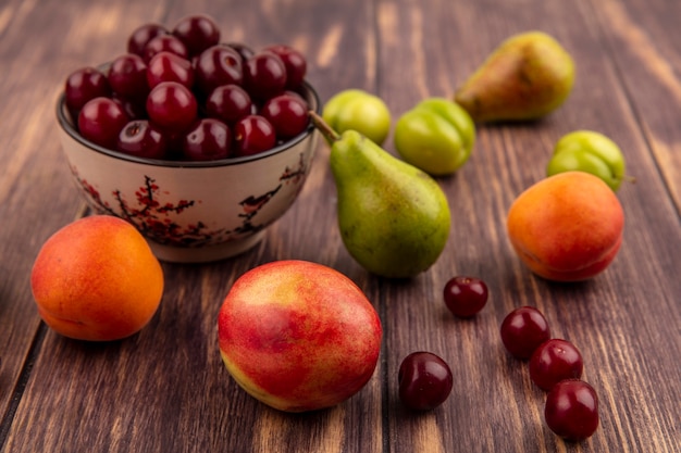ボウルにさくらんぼとしての果物の側面図と木製の背景に桃梅アプリコット梨さくらんぼのパターン
