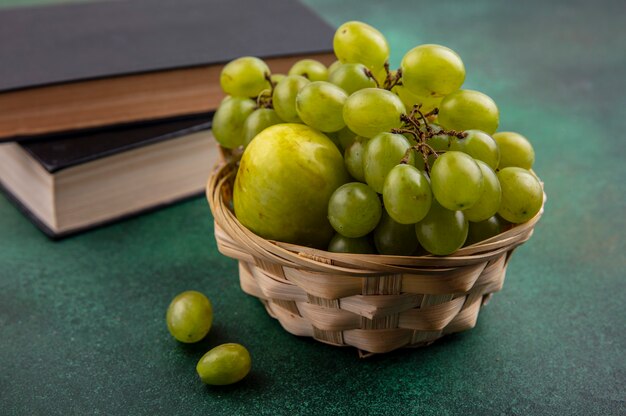 緑の背景に閉じた本とバスケットのブドウとプルオットとして果物の側面図