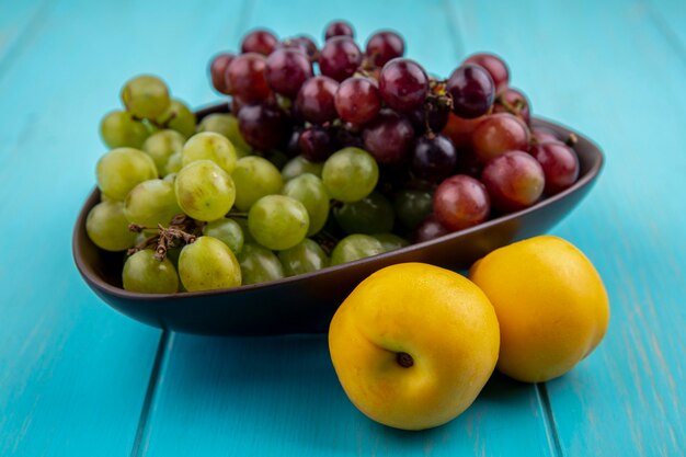 Side view of fruits as nectacots and bowl of grapes on blue background