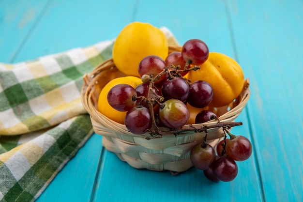 Side view of fruits as nectacots and grape in basket with plaid cloth on blue background