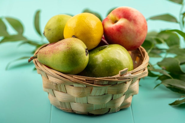 Vista laterale della frutta come pera limone mela pesca nel carrello con foglie su sfondo blu