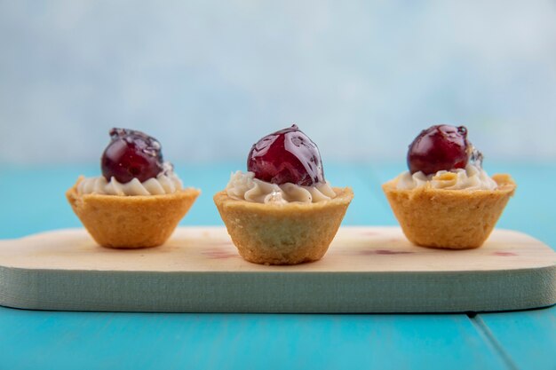 Side view of fruity cupcakes on cutting board on blue surface and gray background