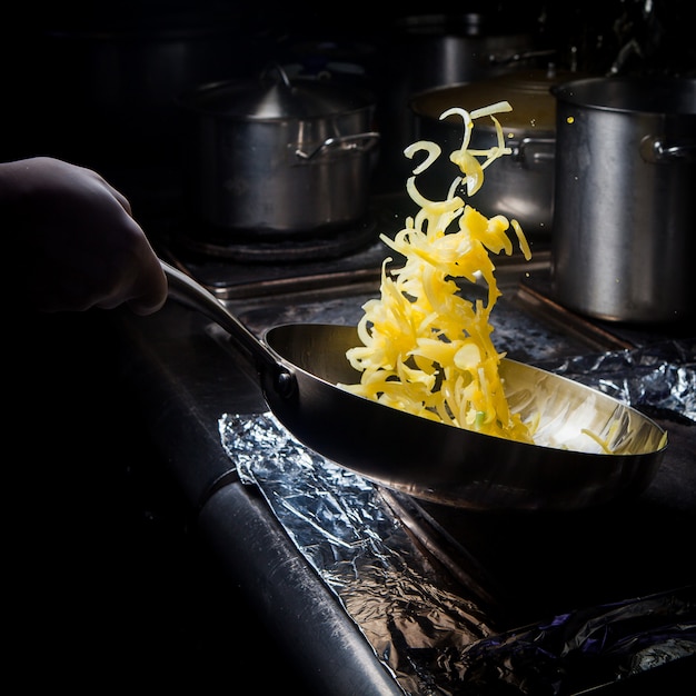 Side view frying onions with pan and human hand in stove