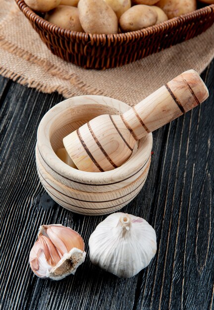 Side view of garlic bulbs and garlic crusher on wooden background