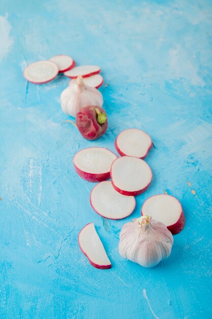 Side view of garlic with sliced and whole radish on blue background with copy space