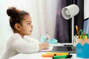 Free photo side view of girl attending online school at home using laptop