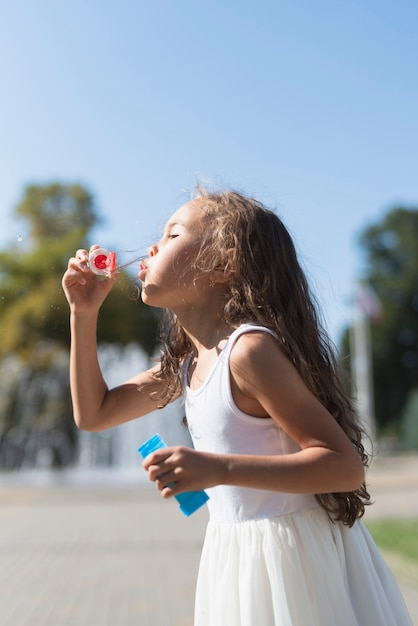 Free photo side view of girl blowing bubbles