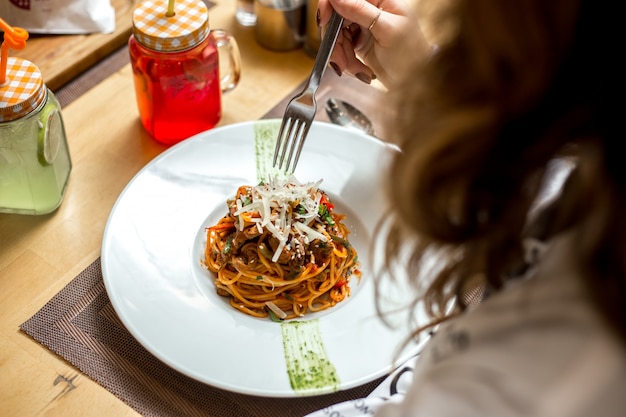 Вид сбоку девочка ест спагетти с мясом и тертым сыром
