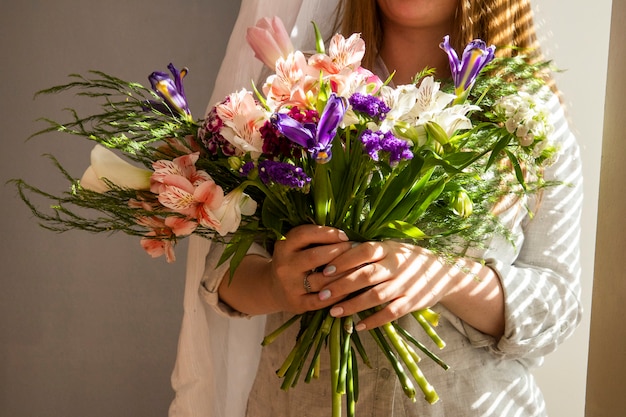 Side view of a girl holding a bouquet of various spring flowers dark purple iris flowers with alstroemeria, pink color tulips , turkish carnation and purple color statice at light table