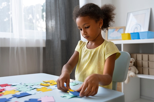 Free photo side view girl making puzzle at table