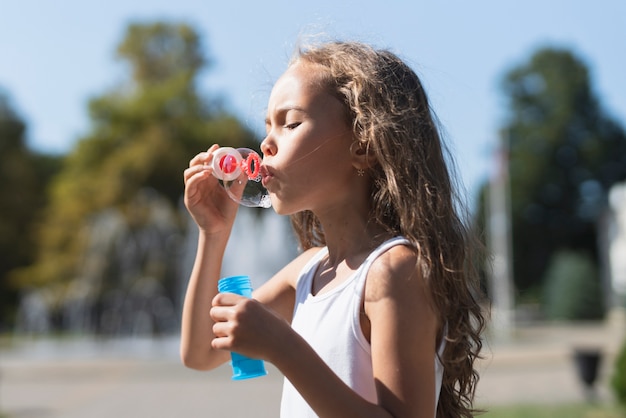 Free photo side view of girl playing with soap bubbles