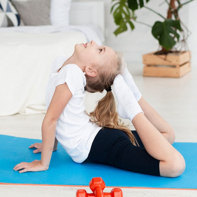 Vista laterale della posa di pratica di yoga della ragazza a casa