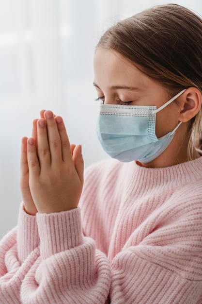 Free photo side view of girl praying with medical mask