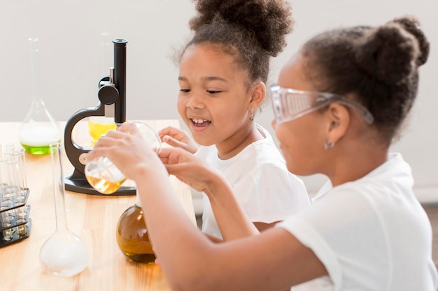 Side view of girl scientists at home with safety glasses and microscope