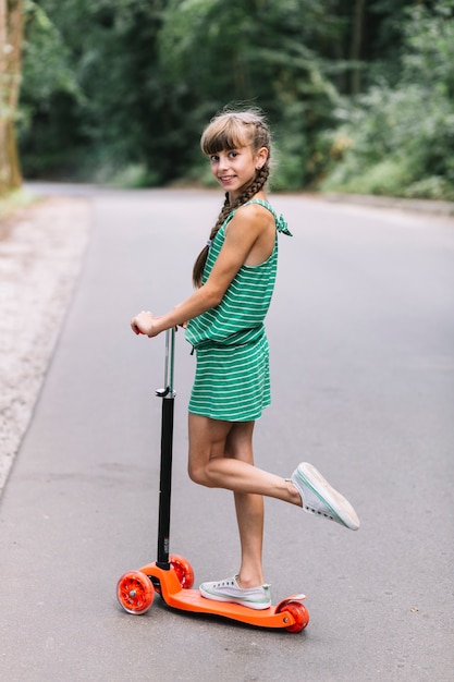 Side view of a girl standing on one leg over the scooter on road