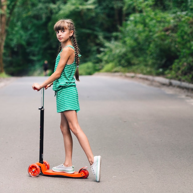 道路上のスクーターの上に立っている少女の側面図