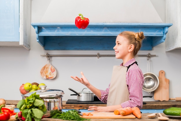 Side view of a girl throwing the red bell pepper in the kitchen
