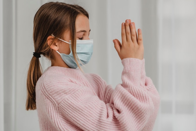 Vista laterale della ragazza con la mascherina medica che prega