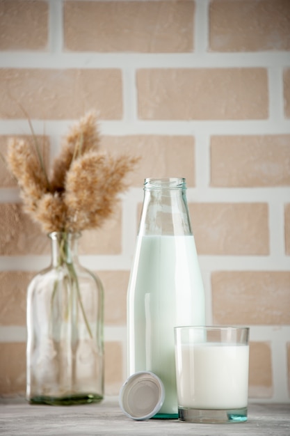 パステルカラーのレンガの背景にミルクキャップで満たされたガラス瓶とカップの側面図