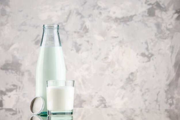 Side view of glass bottle and cup filled with milk cap on the right side on pastel colors background with free space