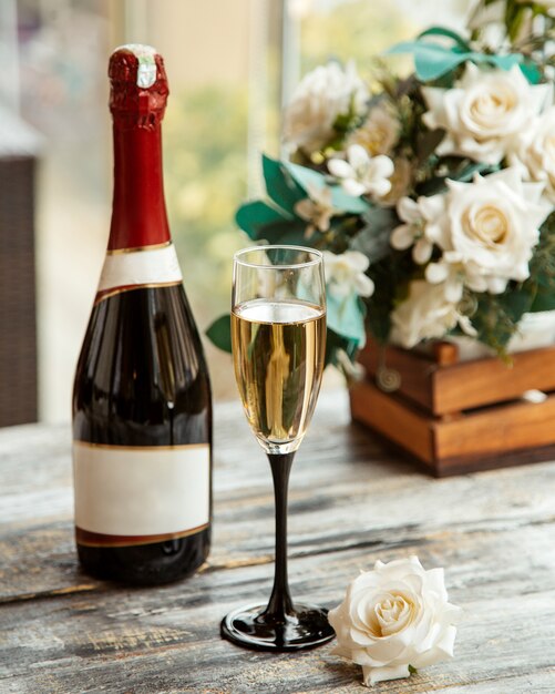 Вид сбоку бокал шампанского с бутылкой и белыми розами