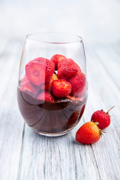 Side view of a glass of chocolate milkshake with strawberries on a grey wooden surface