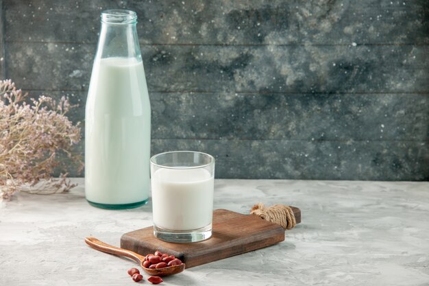 Side view of glass cup on wooden cutting board and bottle filled with milk and peanuts on gray table