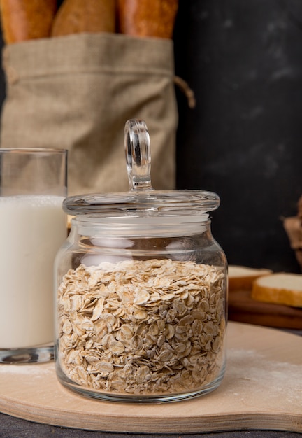 Side view of glass jar with oat-flakes and milk on wooden surface and black background with copy space