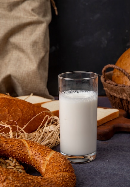 Free photo side view of glass of milk with bagel on maroon surface and black background with copy space