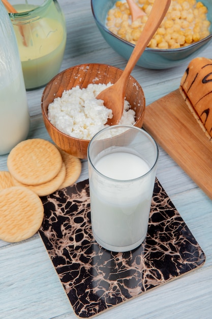 side view of glass of milk with cookies condensed milk cottage cheese roll cereals on wooden table