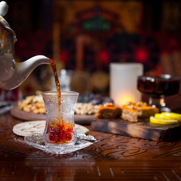 Side view glass of tea with baklava and lemon and jam in table