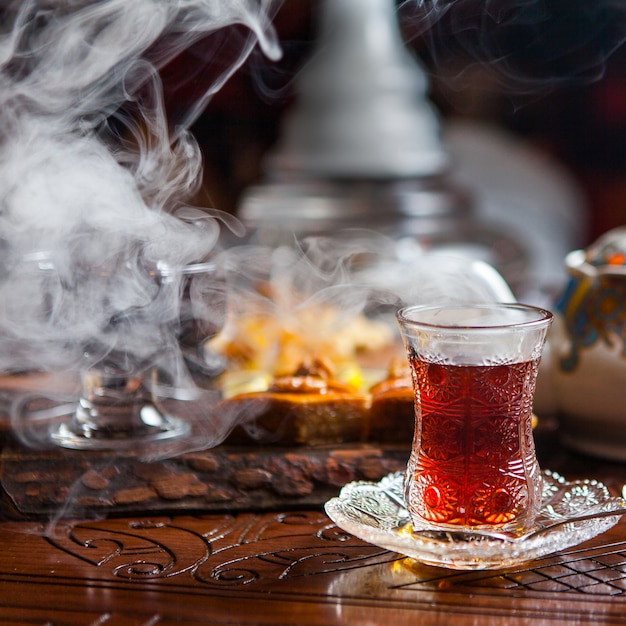 Side view glass of tea with baklava and smoke in table