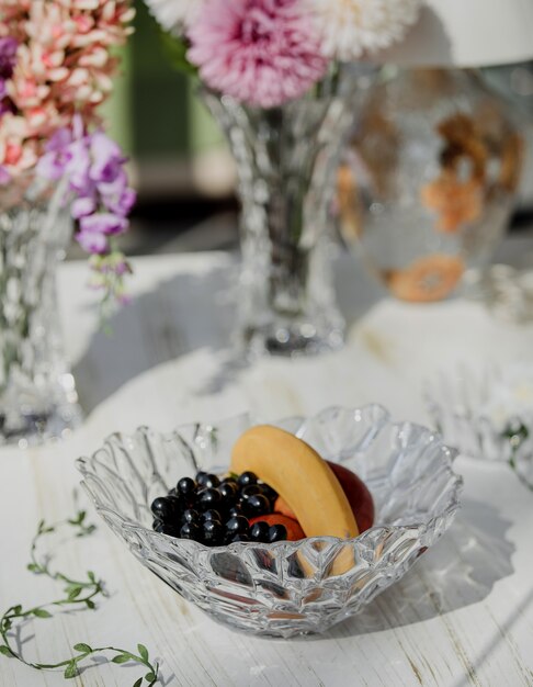 Side view of glass vase with fruit grape and bananas on a white wooden table