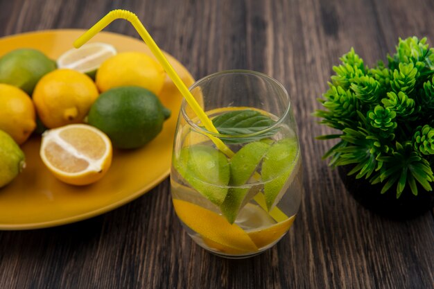 Side view glass of water with lemon slices with lime and yellow straw on wooden background